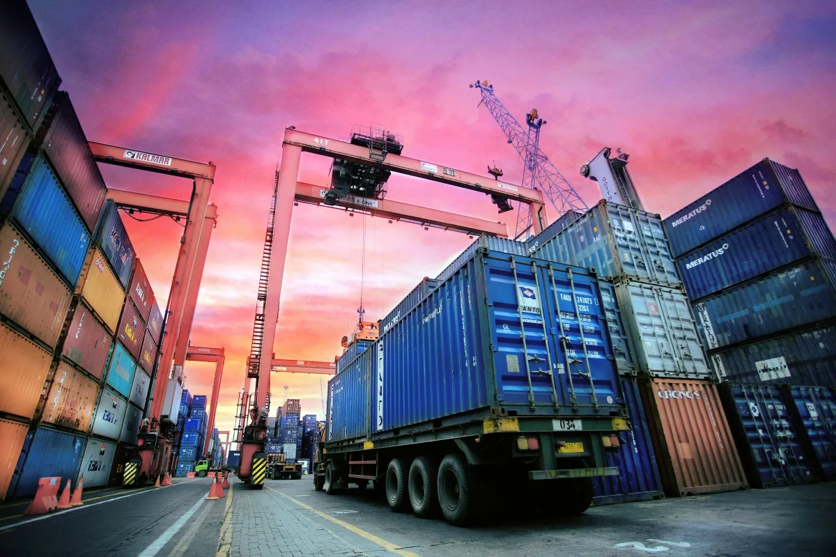Container truck under a gantry crane in a container yard at sunset