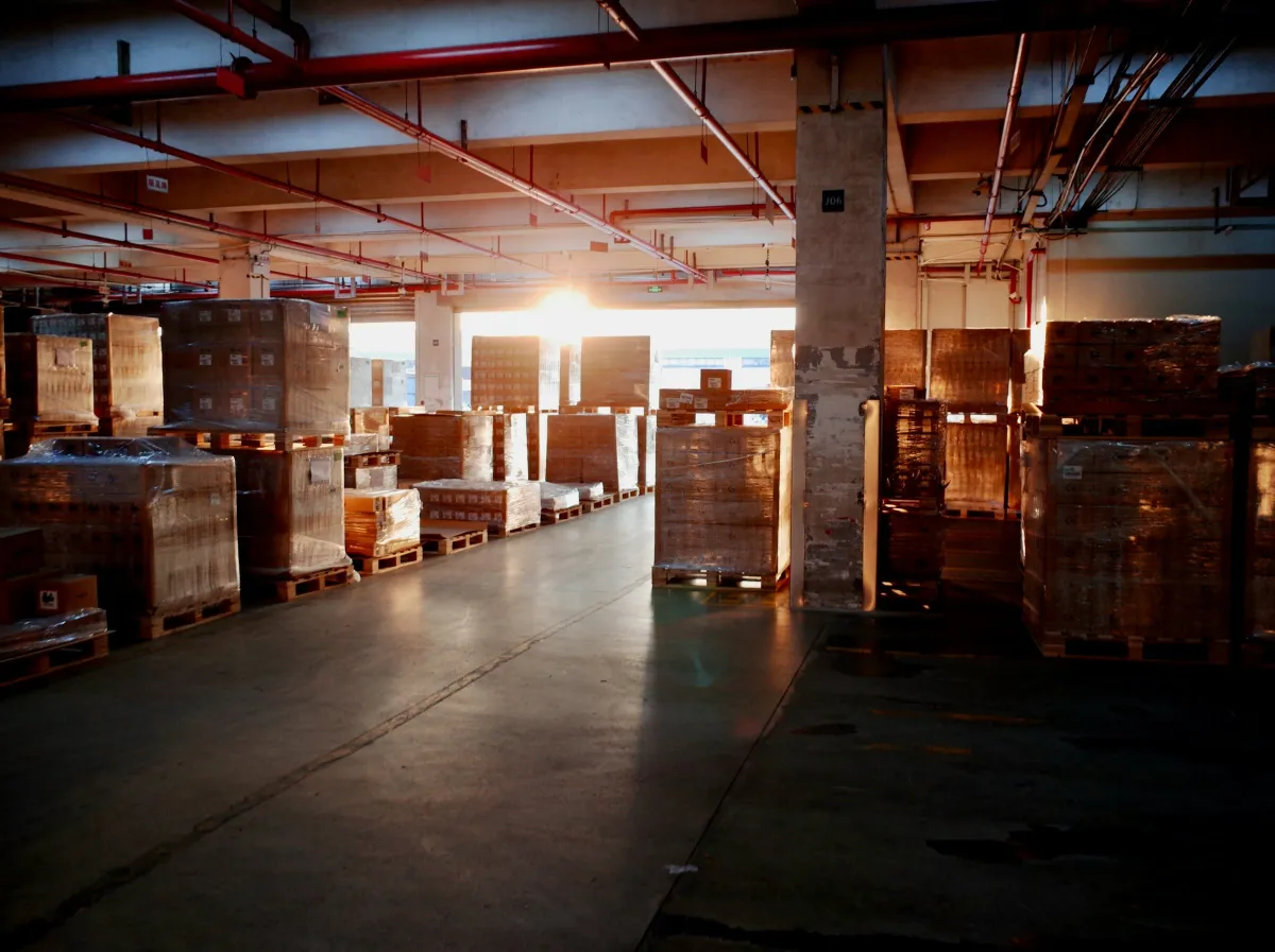 Warehouse floor with wrapped pallets of goods and sunlight at the loading door