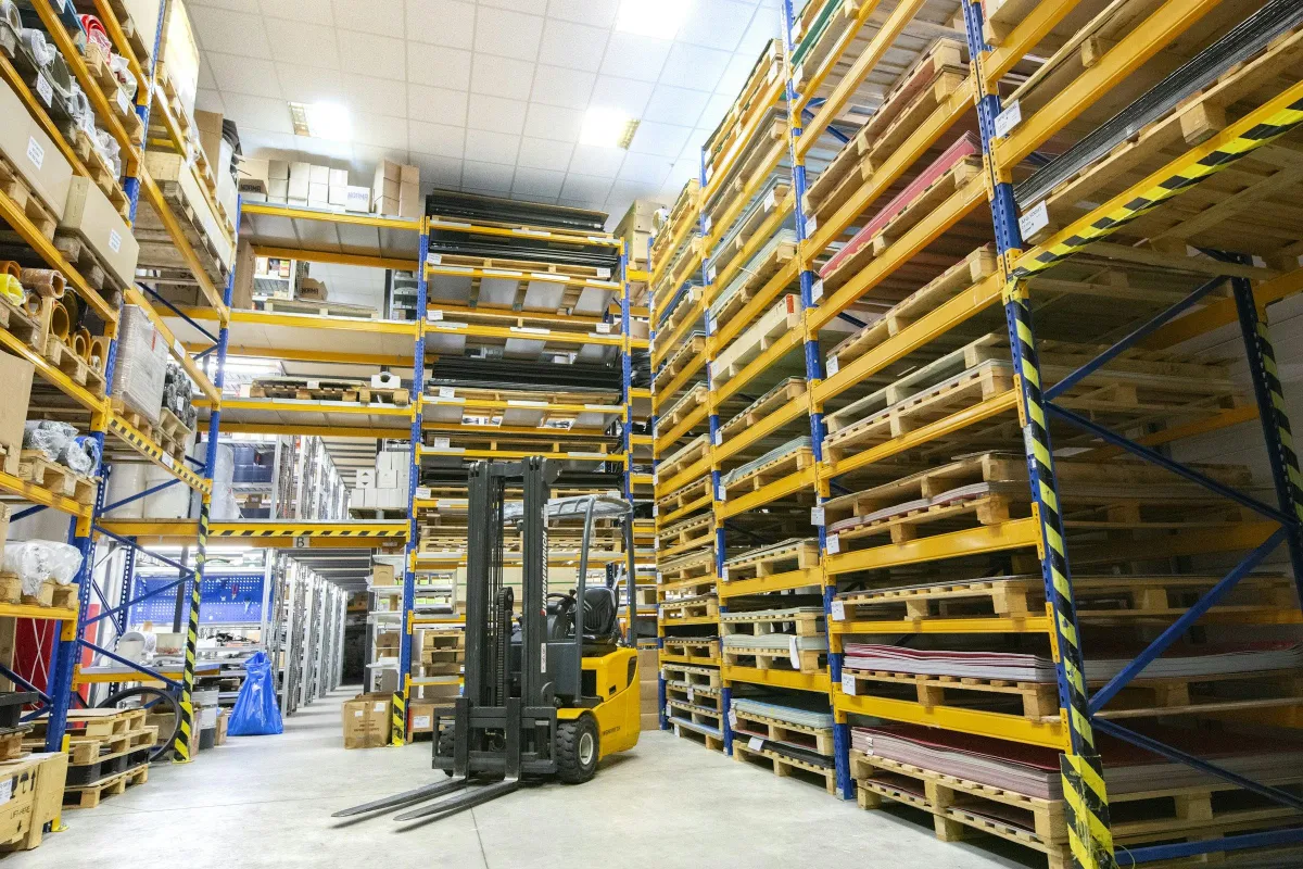 Forklift di lorong gudang di antara rak palet yang tinggi