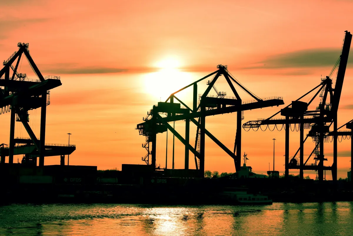 Silhouetted container cranes against an orange sunset over the water